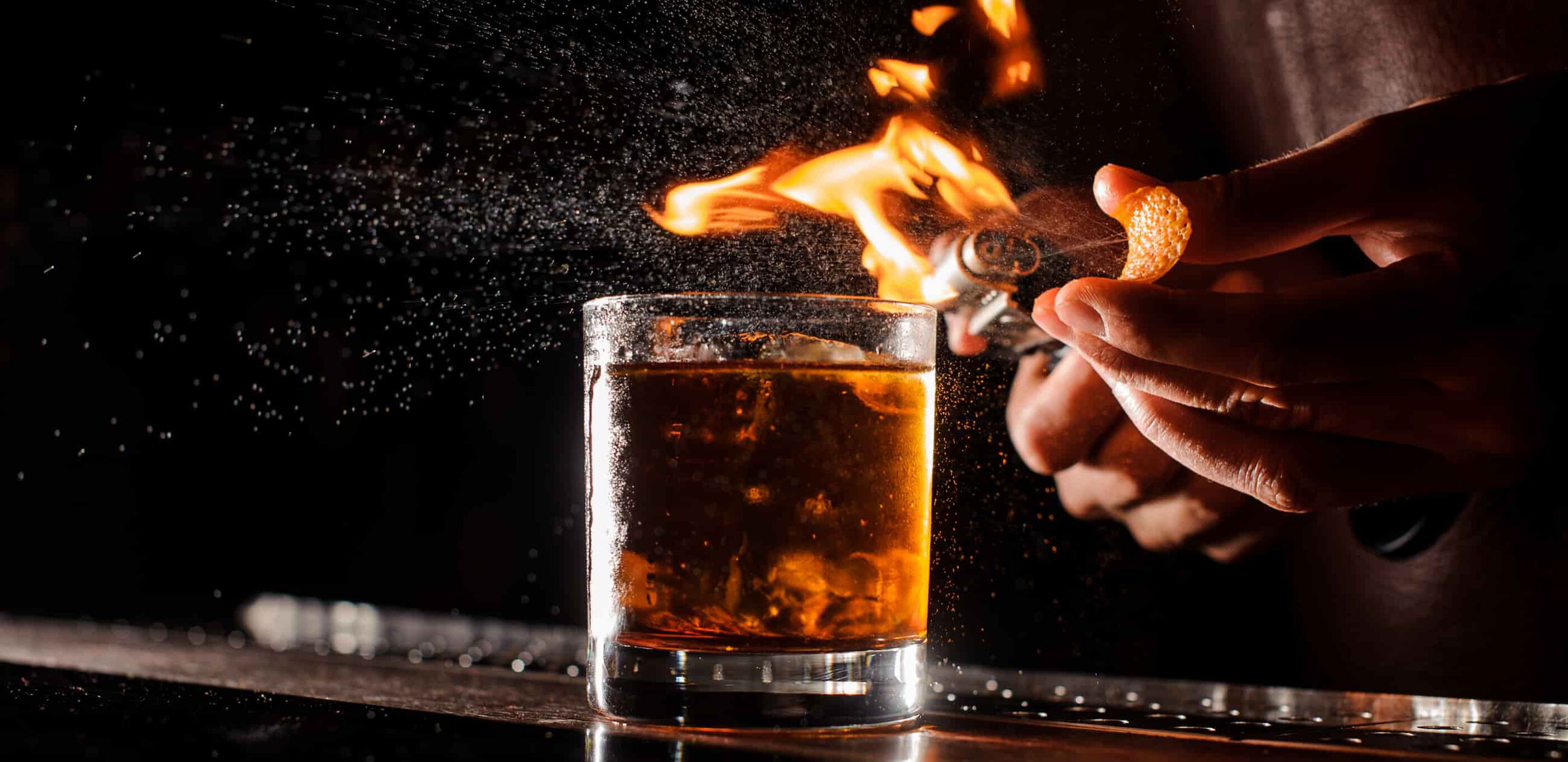 An orange peel is spritzed through a flame over an Old Fashioned